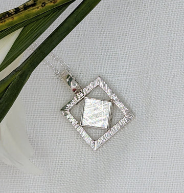 Diamond shaped meteorite slice dangling within a silver hammered texture square pendant hanging on a rope chain