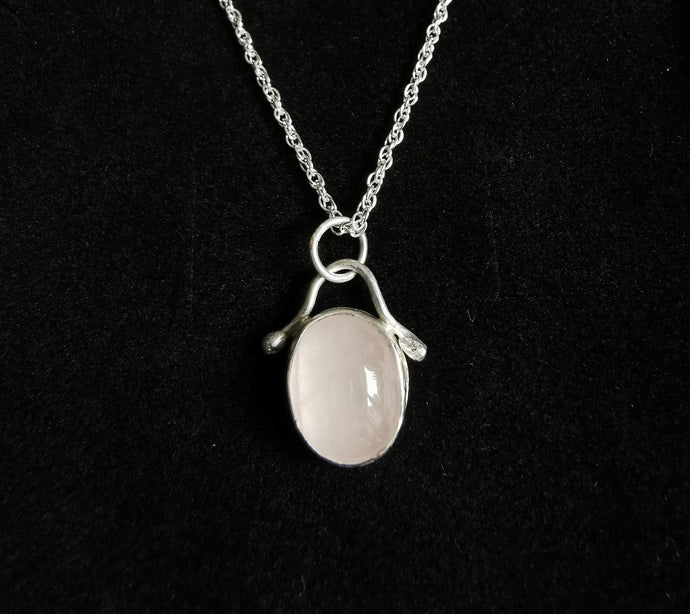 Polished oval rose quartz pendant with silver embellishment hanging on a silver rope chain
