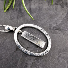 Load image into Gallery viewer, Long rectangular meteorite slice dangling within a silver oval pendant on a rope chain
